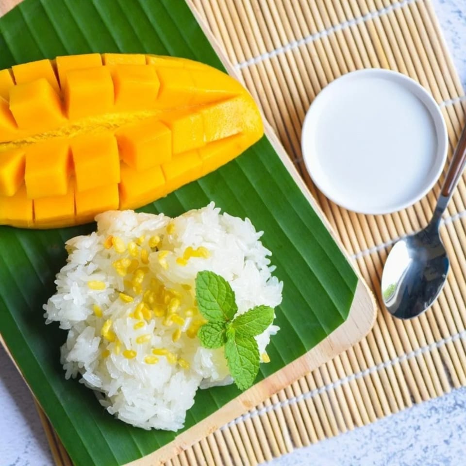 Thai mango sticky rice with coconut milk and mint on a banana leaf.