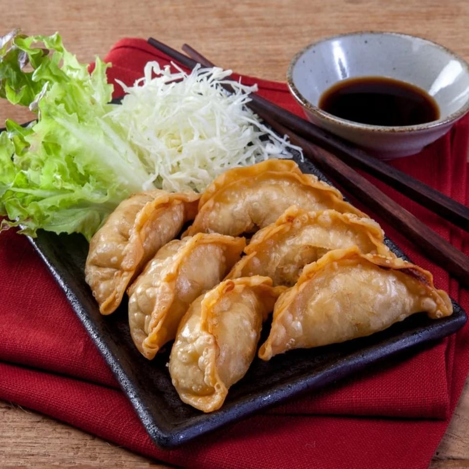 Golden fried Thai dumplings with shredded cabbage, lettuce, and soy sauce on a black plate.